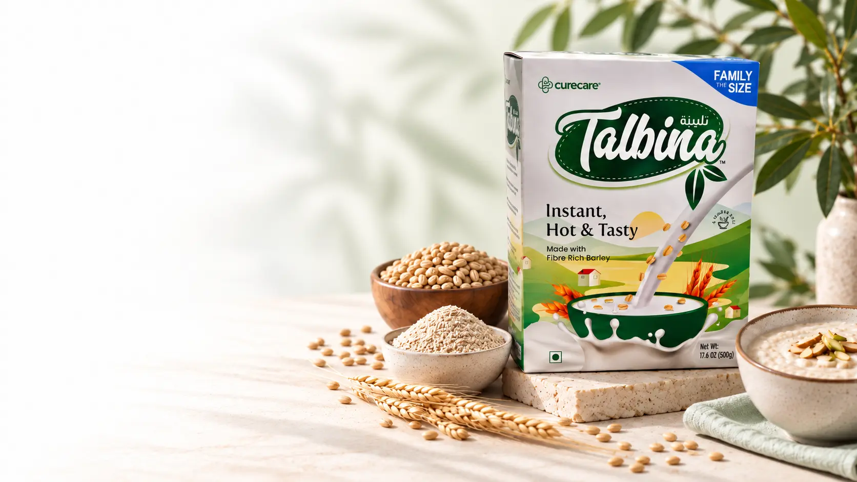 A box of Talbina instant barley porridge on a stone slab, beside bowls of barley grains, barley flour and prepared talbina, with wheat stalks and green leaves.